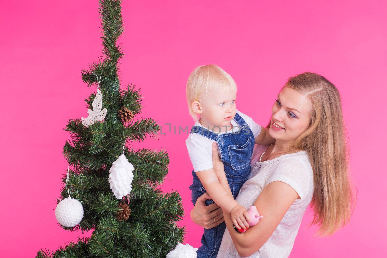 Holidays, family and christmas concept - young mom with her little daughter near christmas tree on pink background by Satura86