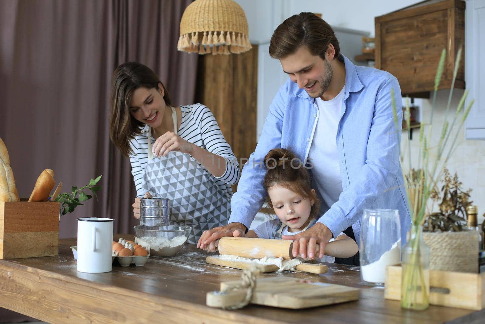 Cute little girl and her parents are having fun while cooking in kitchen at home together