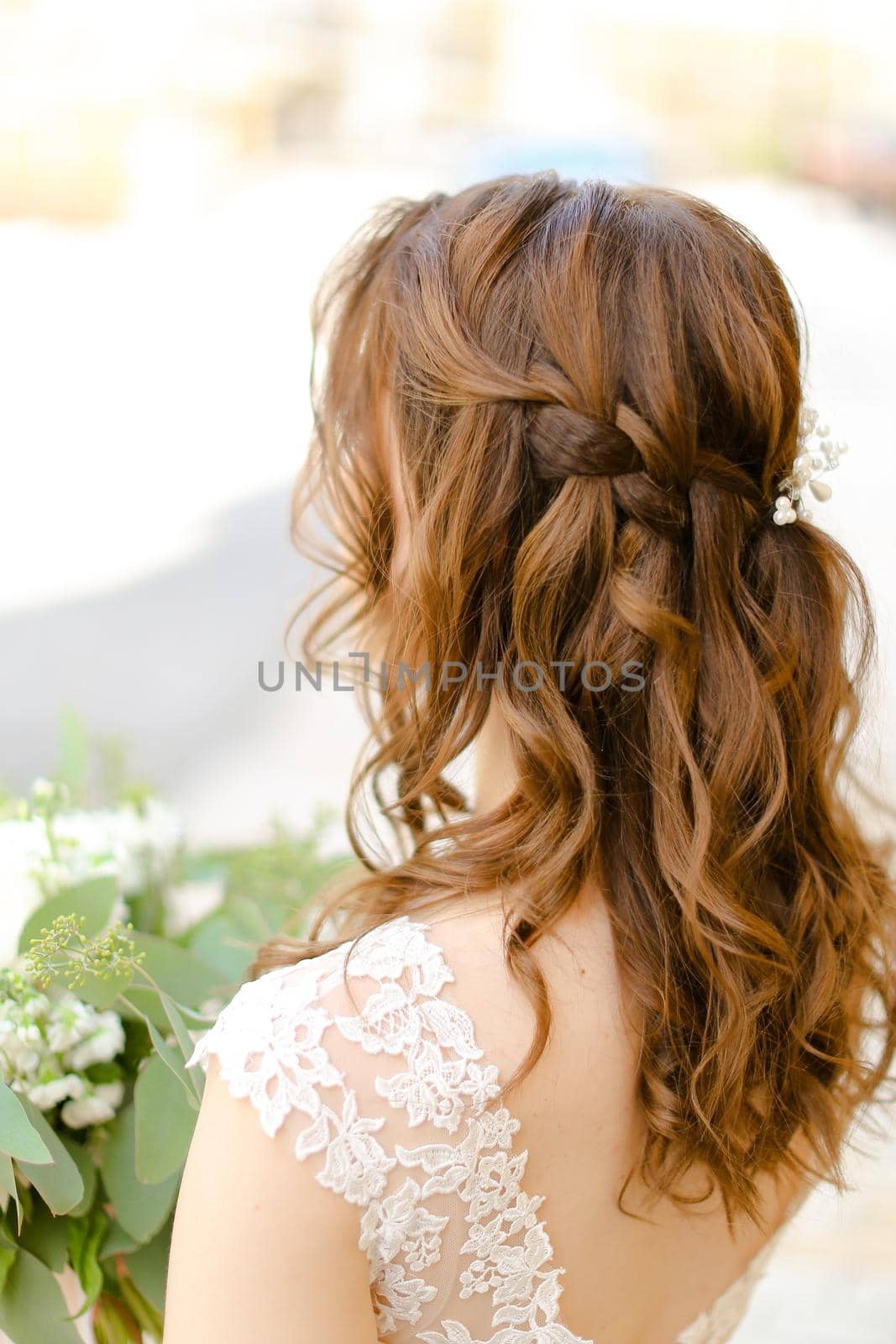 Back view of brown curls for bride keeping flowers. Concept of wedding photo session and stylish hair do.