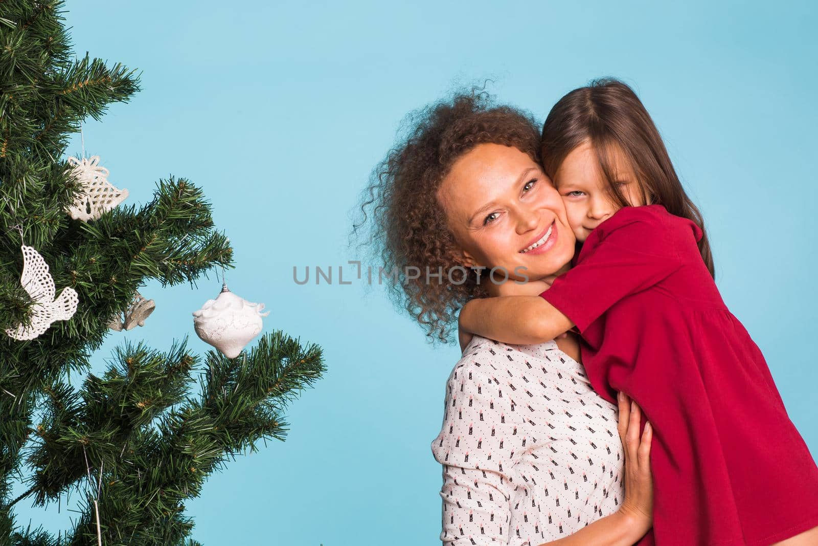 Christmas of young mom and her daughter with Christmas tree on blue background.