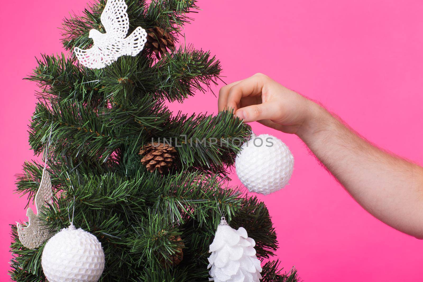 December and holidays concept - Man's hand decorating Christmas Tree on pink background by Satura86