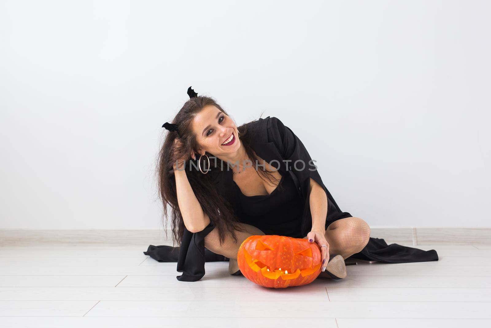 Happy gothic young woman in witch halloween costume smiling over white room background by Satura86