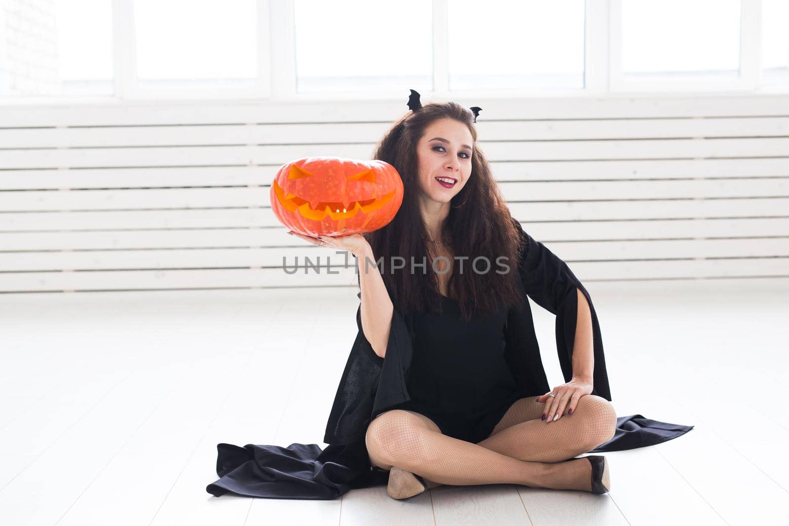 Excited happy young woman in halloween costume posing with carved pumpkin in lightroom by Satura86