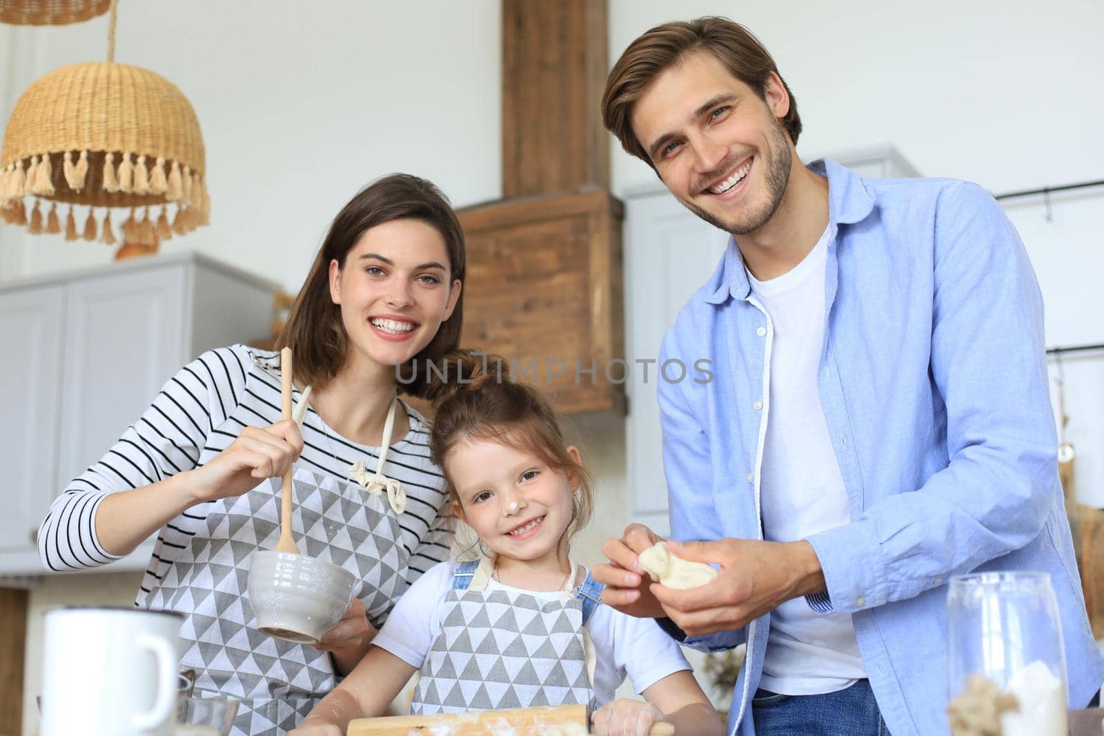 Cute little girl and her parents are having fun while cooking in kitchen at home together