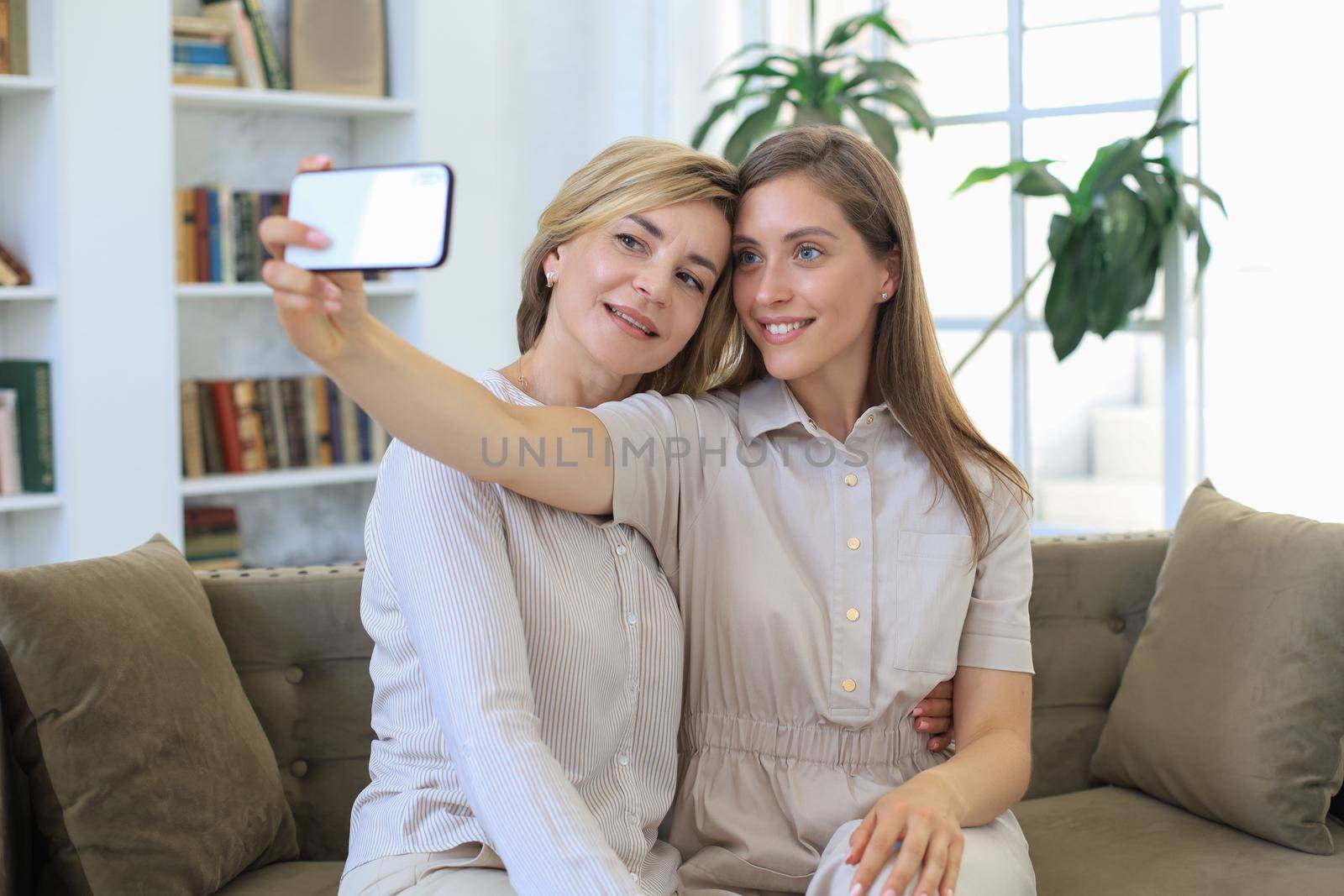 Happy middle aged mother and daughter taking selfie at home