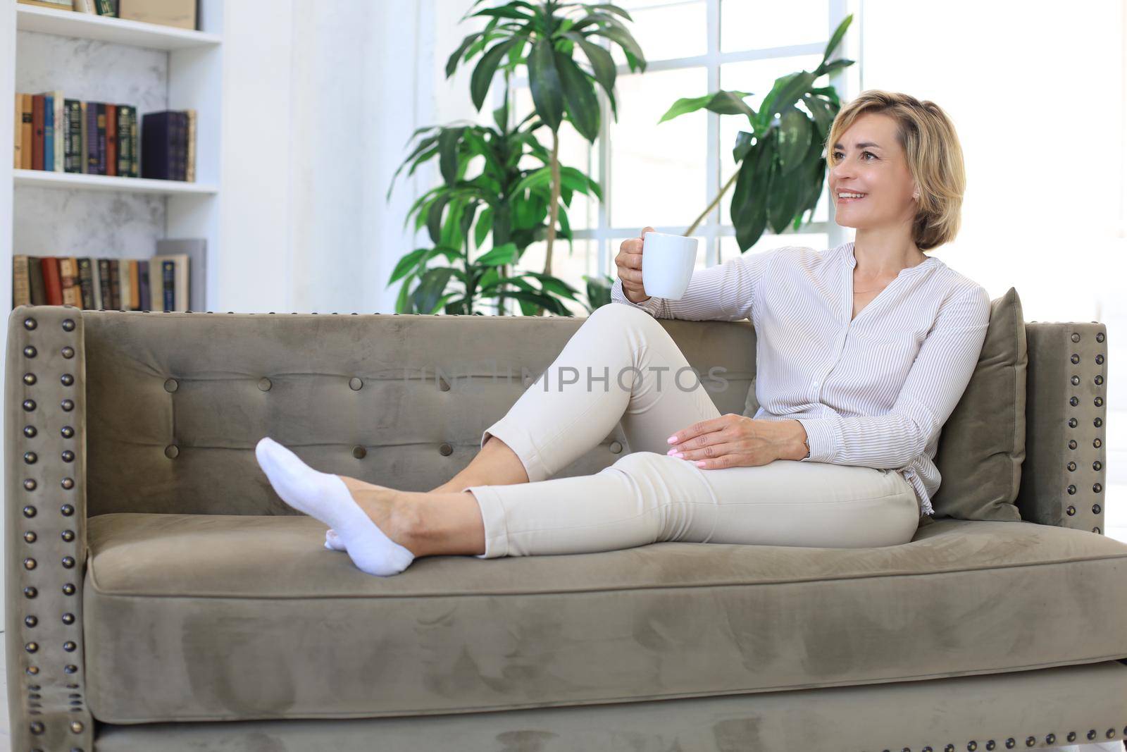 Mature blond woman in couch having a tea or coffee