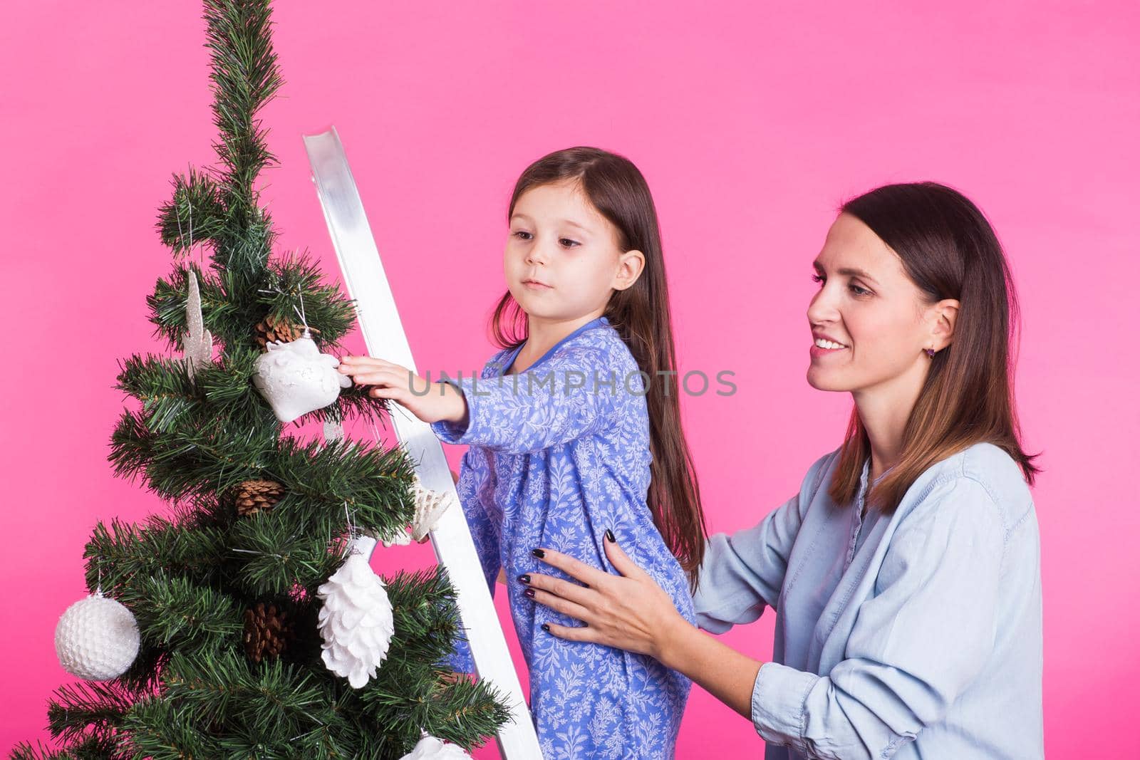 Christmas of young mom and her daughter with Christmas tree on pink background.