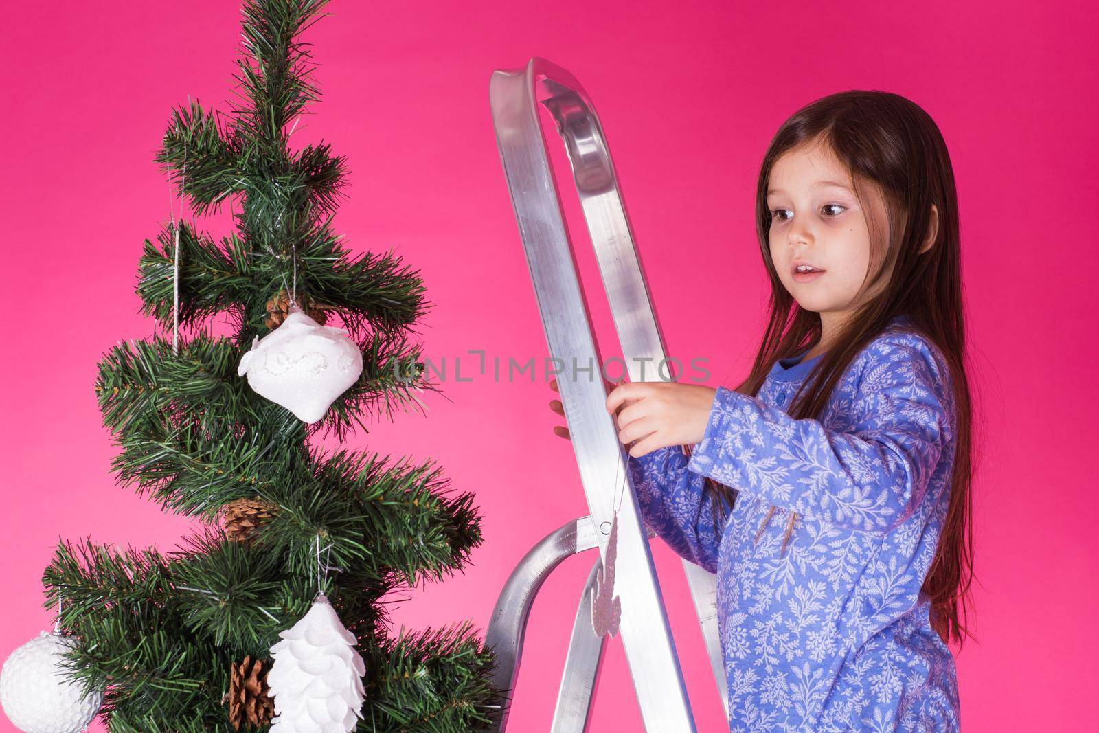 Little girl with christmas tree on pink background.