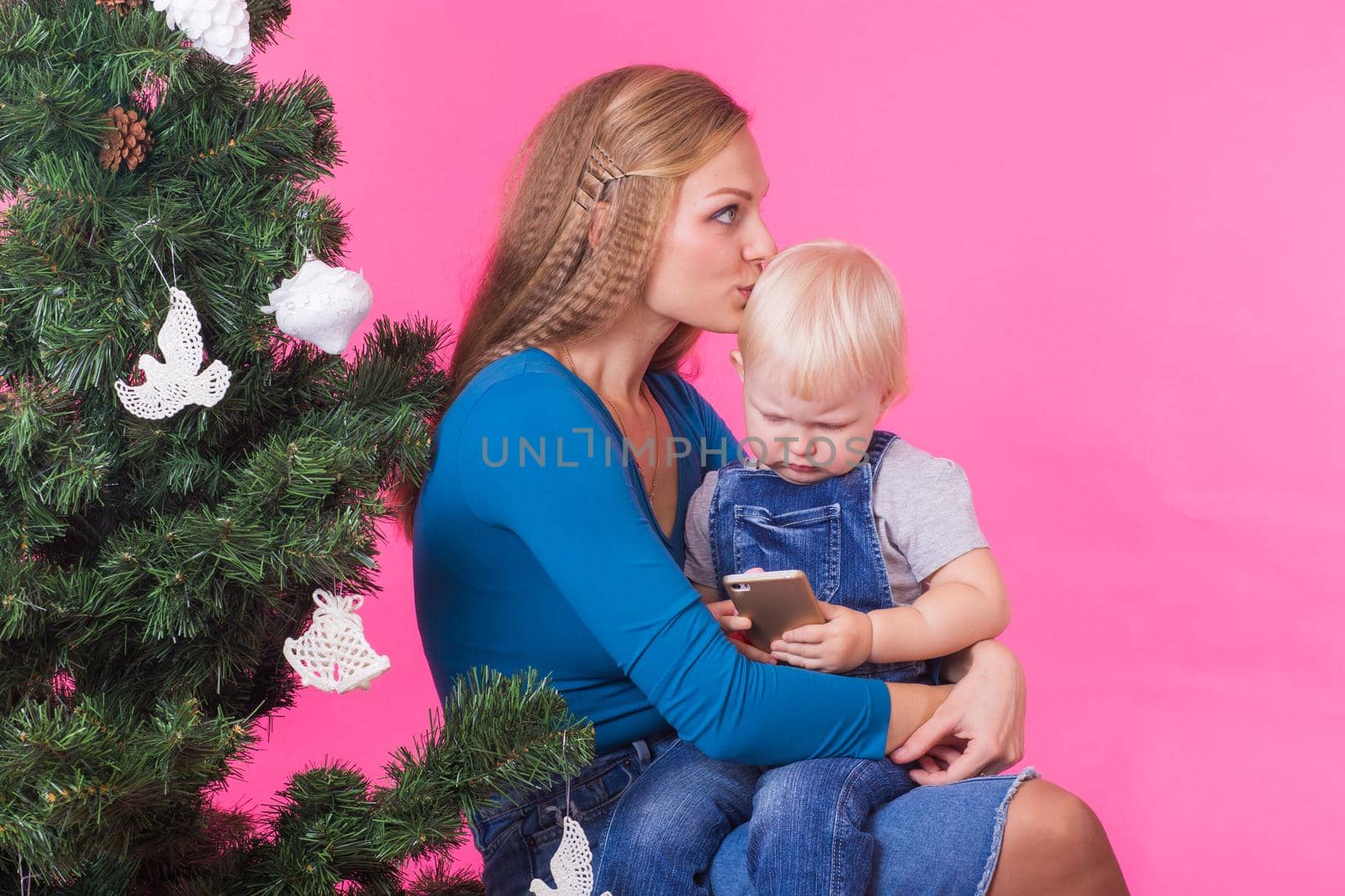 Christmas and holiday concept - Portrait of smiling woman holding her little daughter near Christmas tree on pink background.