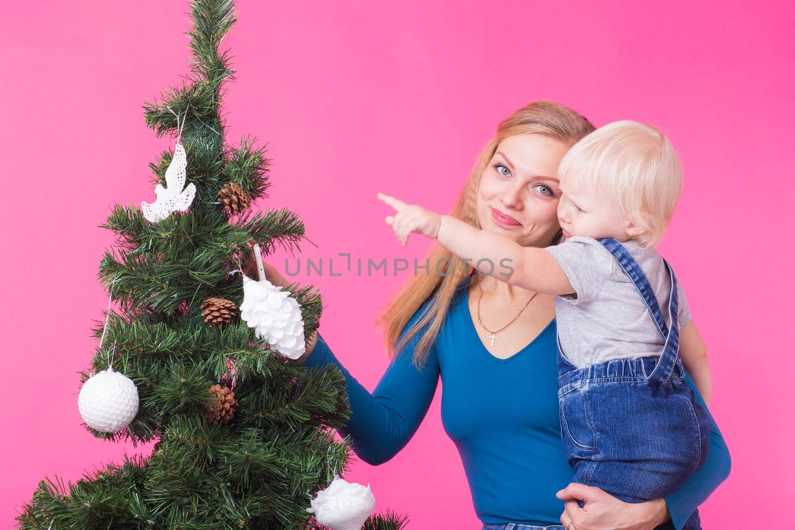 Christmas, holidays and people concept - young happy woman with her daughter on hands show decorations on christmas tree.