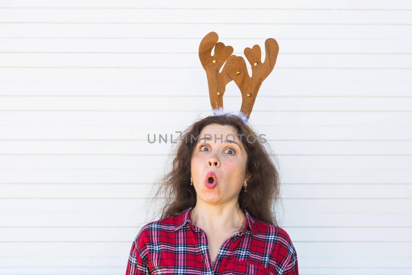 Holiday, Christmas and people concept - Surprised woman with deer horns over white background.