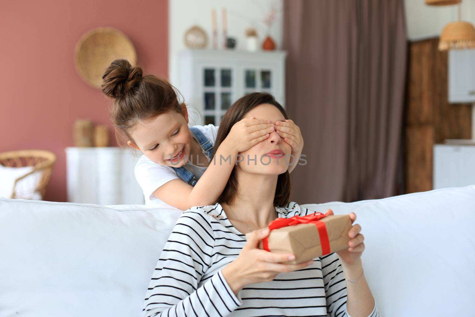 Little girl make birthday present to excited parent , smiling little child congratulate give gift box to happy mother and closed mother's eyes