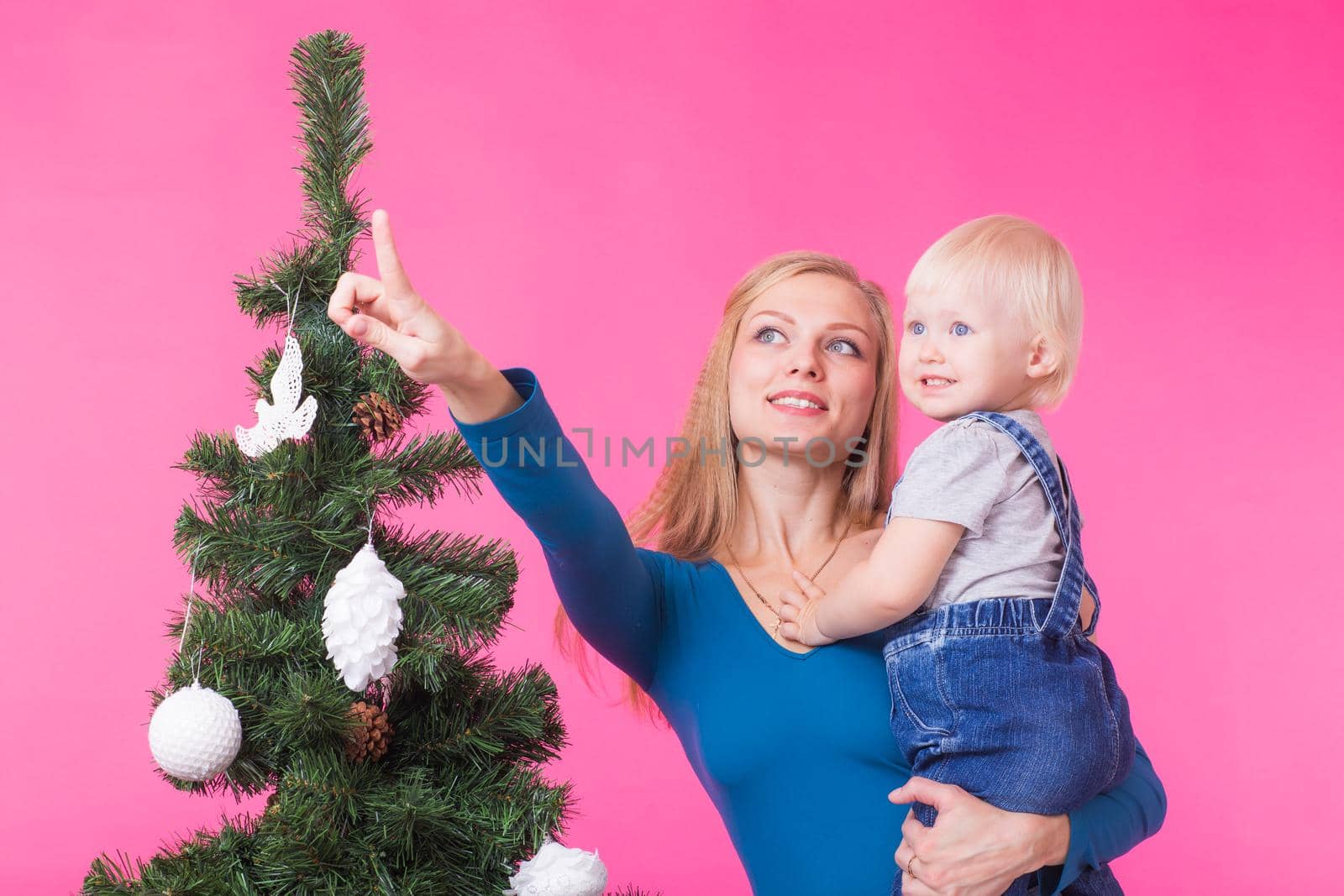 Christmas, holidays and people concept - young happy woman with her daughter on hands show decorations on christmas tree by Satura86