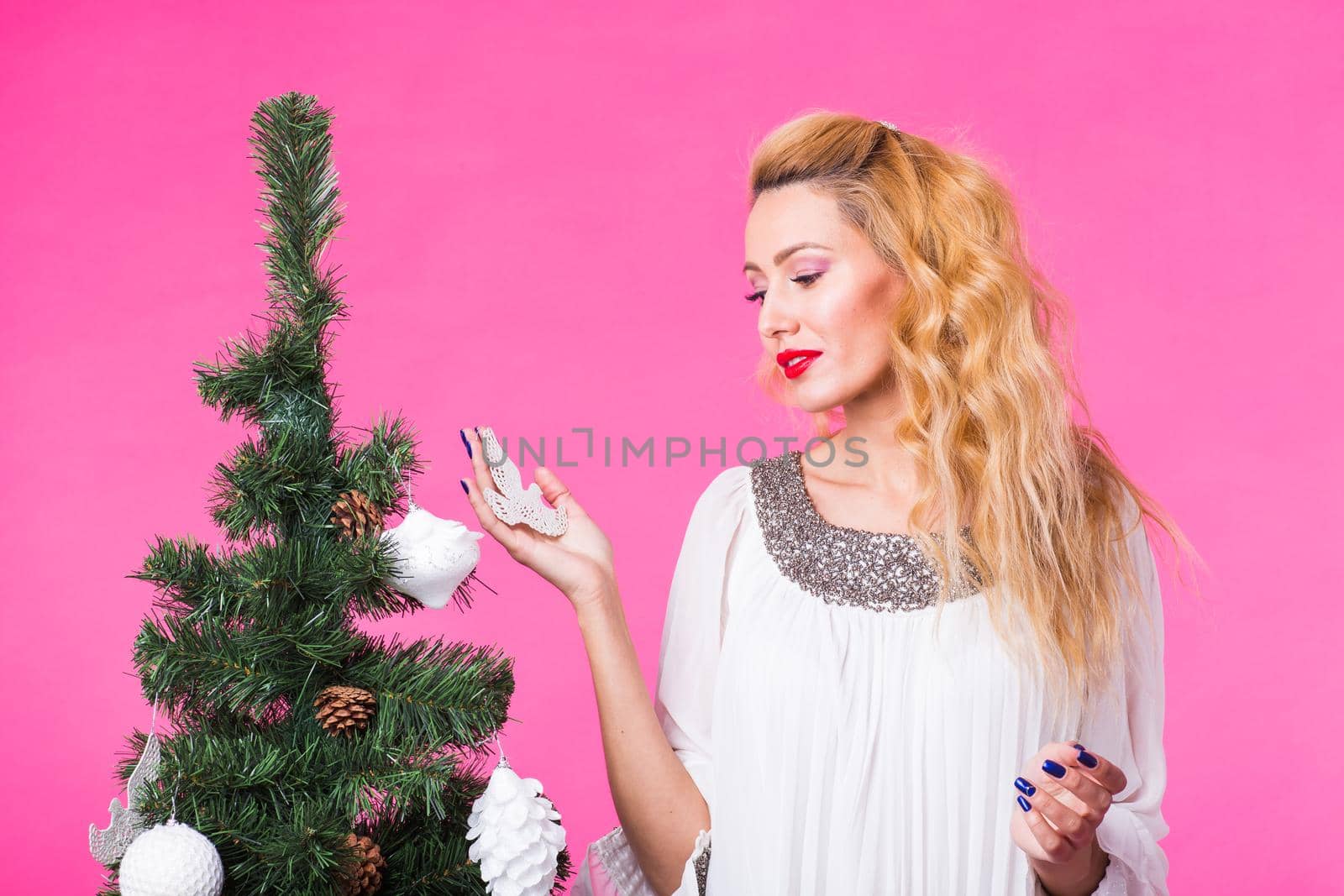 People, holidays and christmas concept - woman decorating christmas tree on pink background by Satura86
