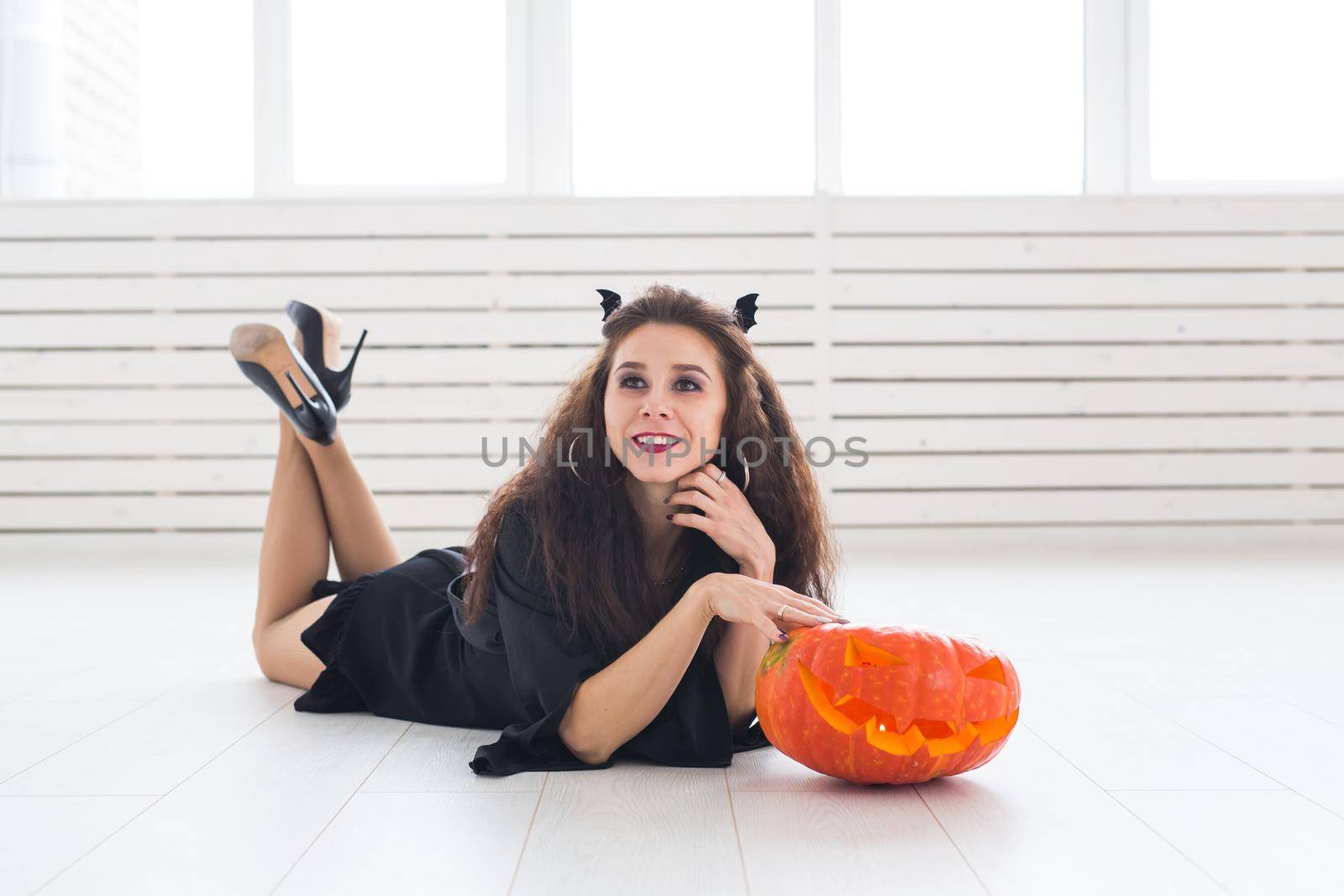 Happy gothic young woman in witch halloween costume smiling over white room background.