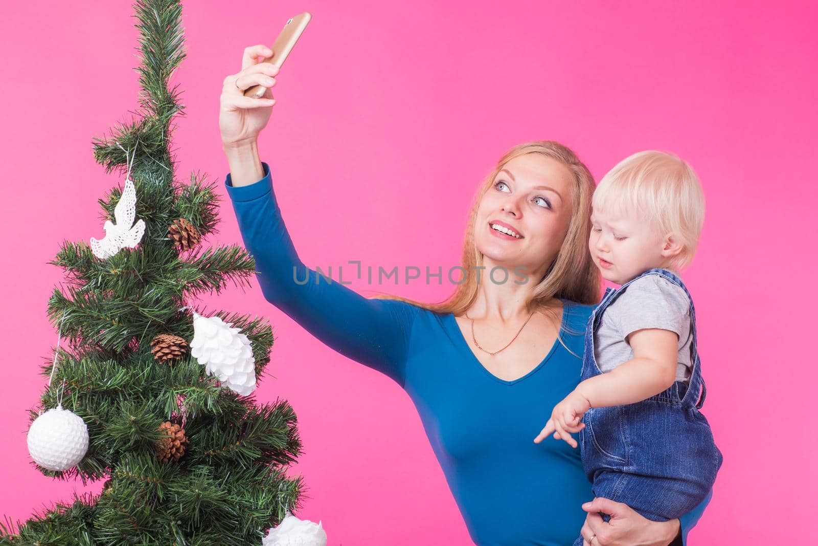 Mother and little daughter taking a selfie near Christmas tree.