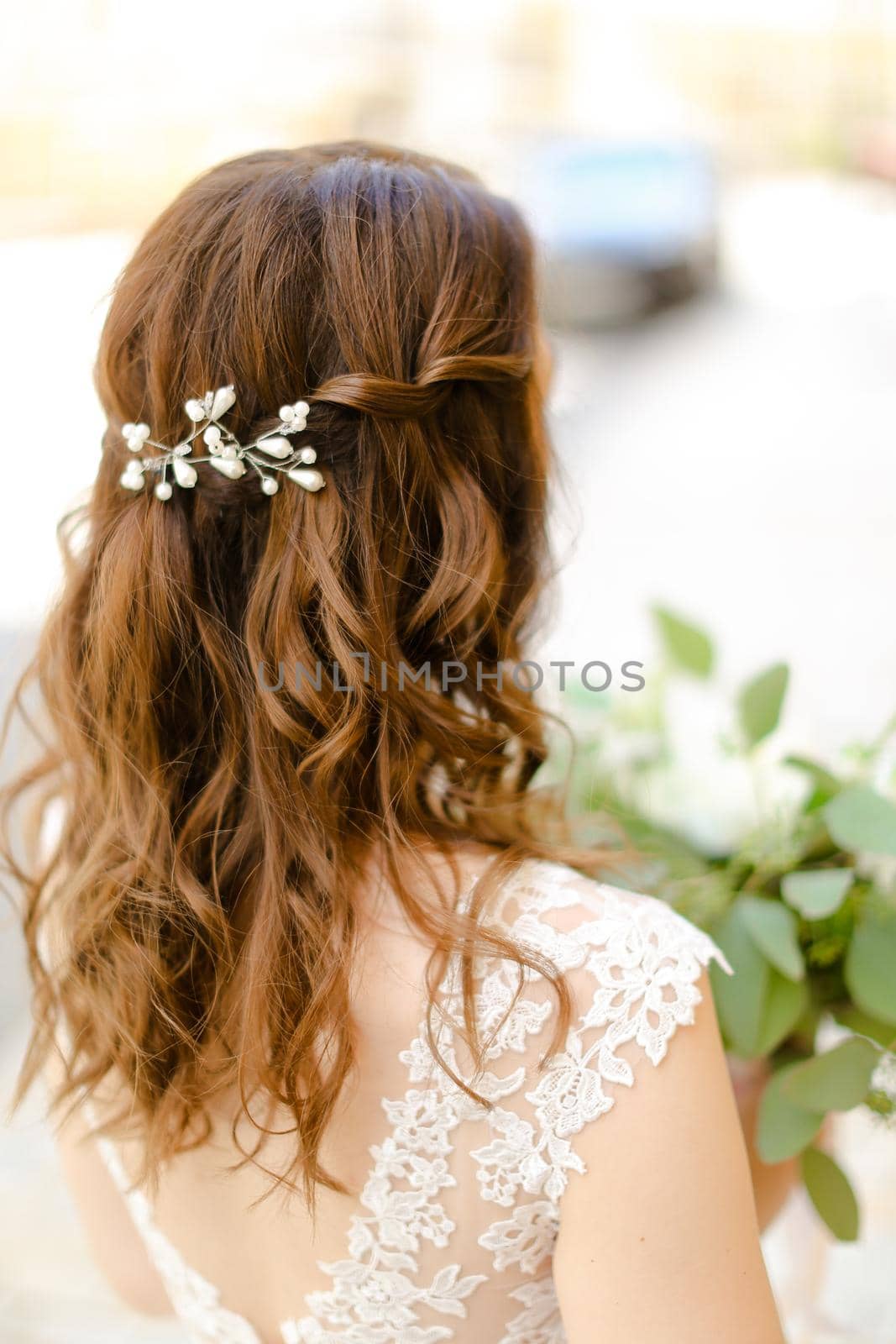 Back view of nice brown curls for bride keeping flowers. Concept of wedding photo session and stylish hair do.