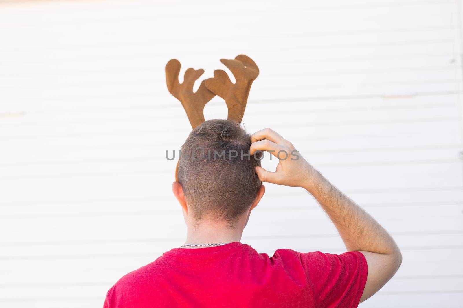 Christmas, holidays and people concept - a man's head with deer horns on it. Man scratches his head.