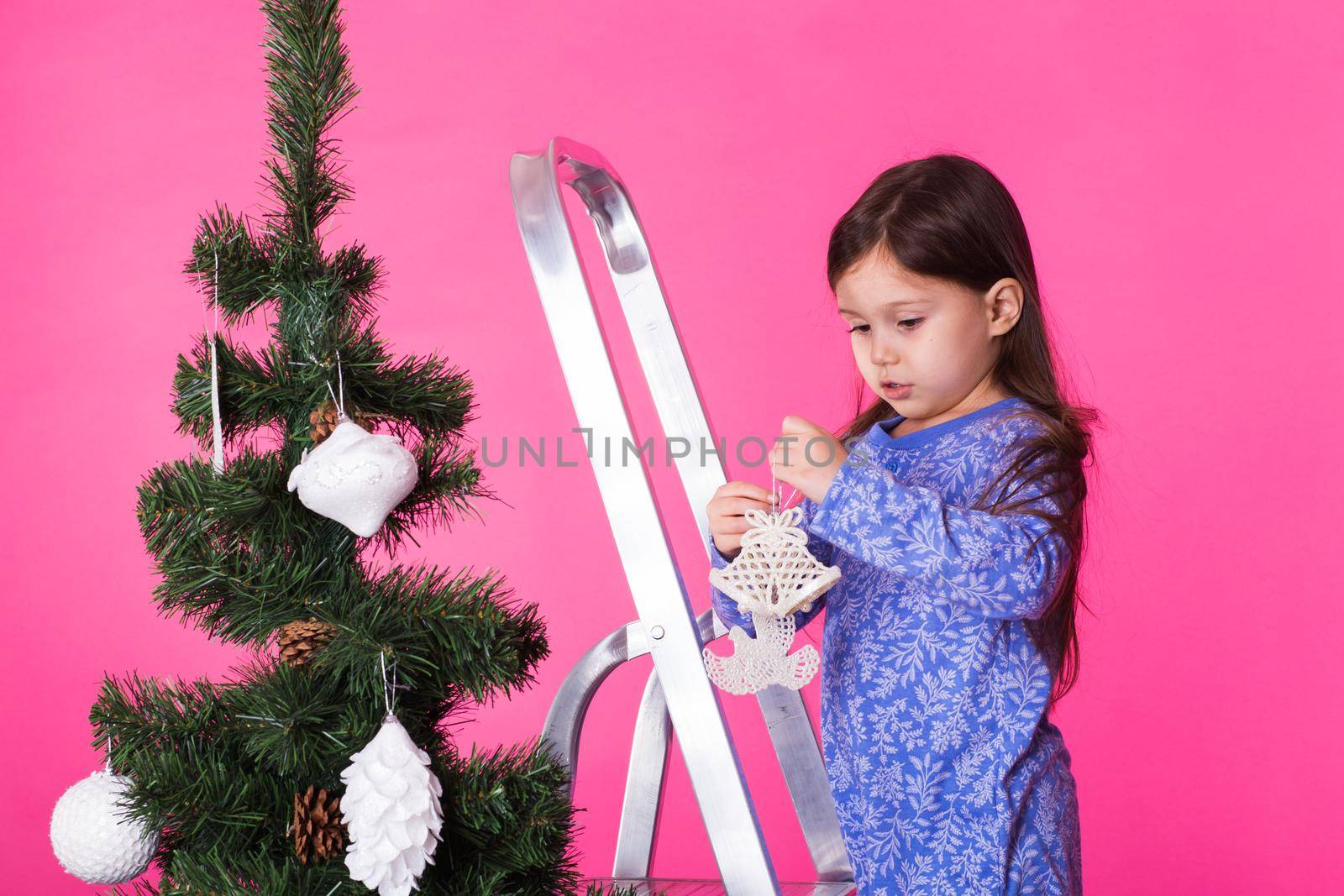 Little girl with christmas tree on pink background.