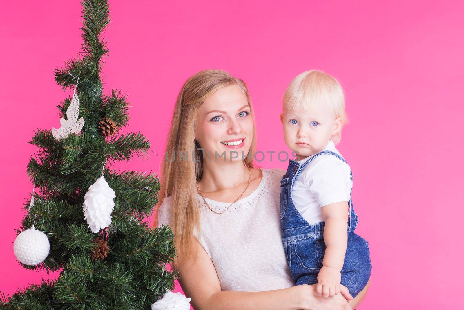 Christmas and holiday concept - Portrait of smiling woman with her little daughter decorating Christmas tree over pink background.