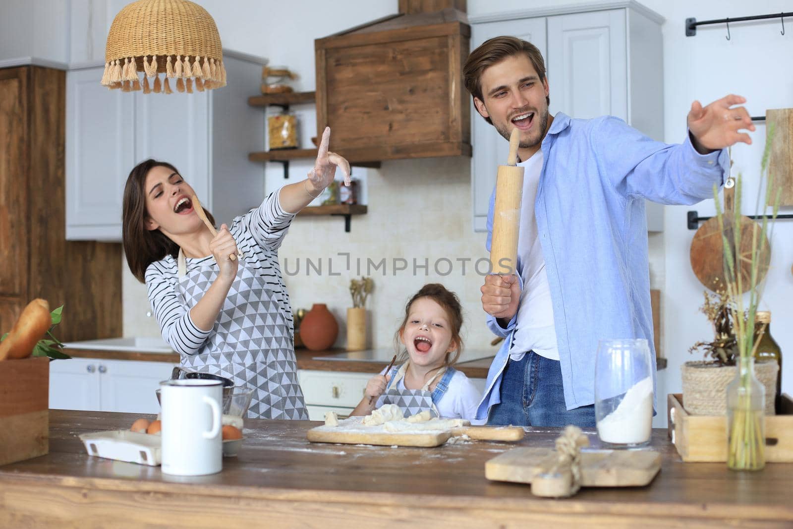 Cute little girl and her parents are having fun while cooking in kitchen at home together
