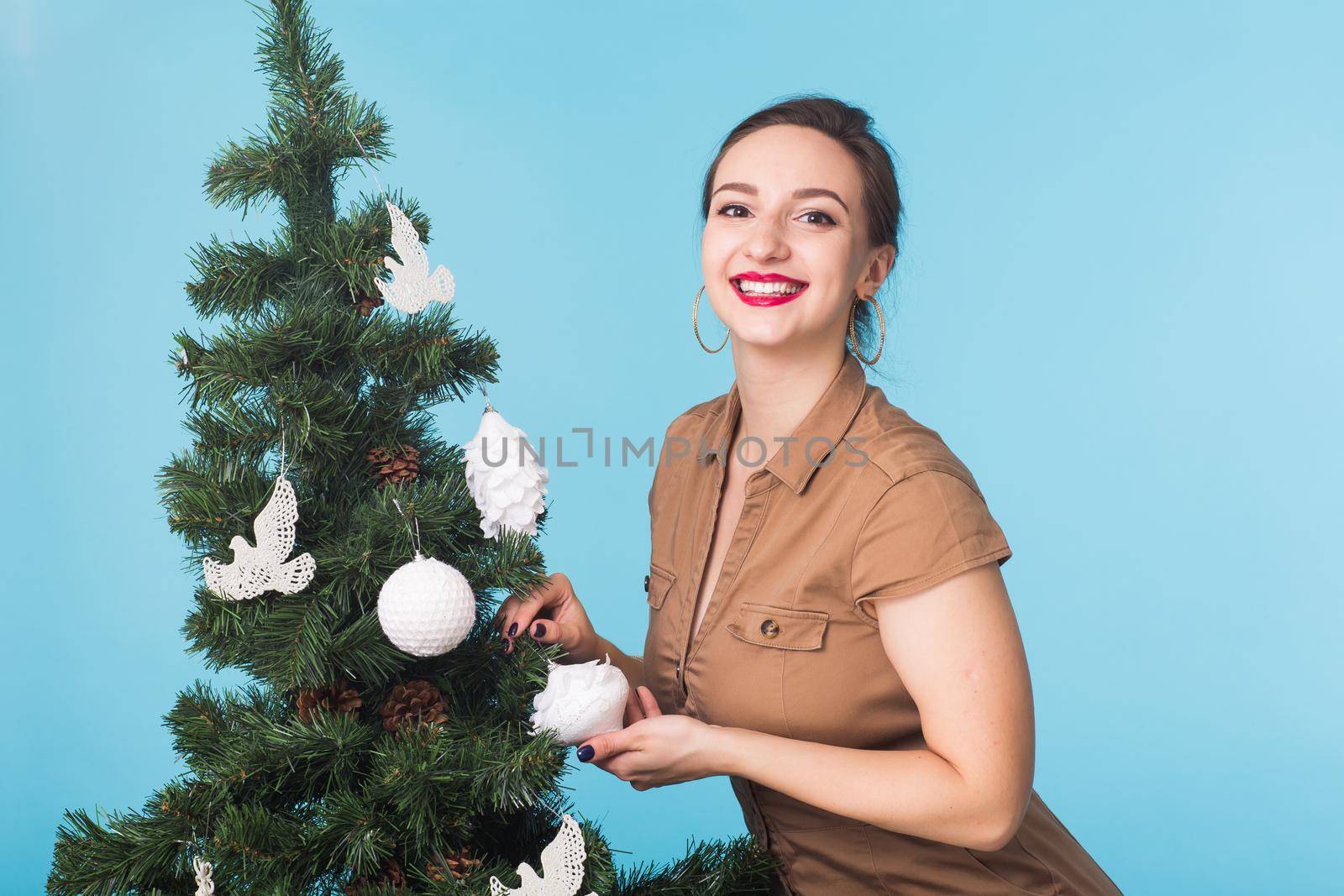Christmas, holidays and people concept - young happy woman decorating christmas tree on blue background by Satura86