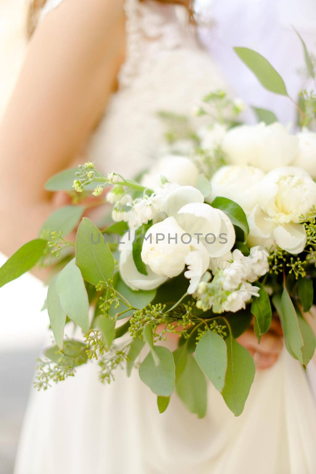 Happy groom hugging beautiful fiancee keeping flowers and wearing white dress. by sisterspro