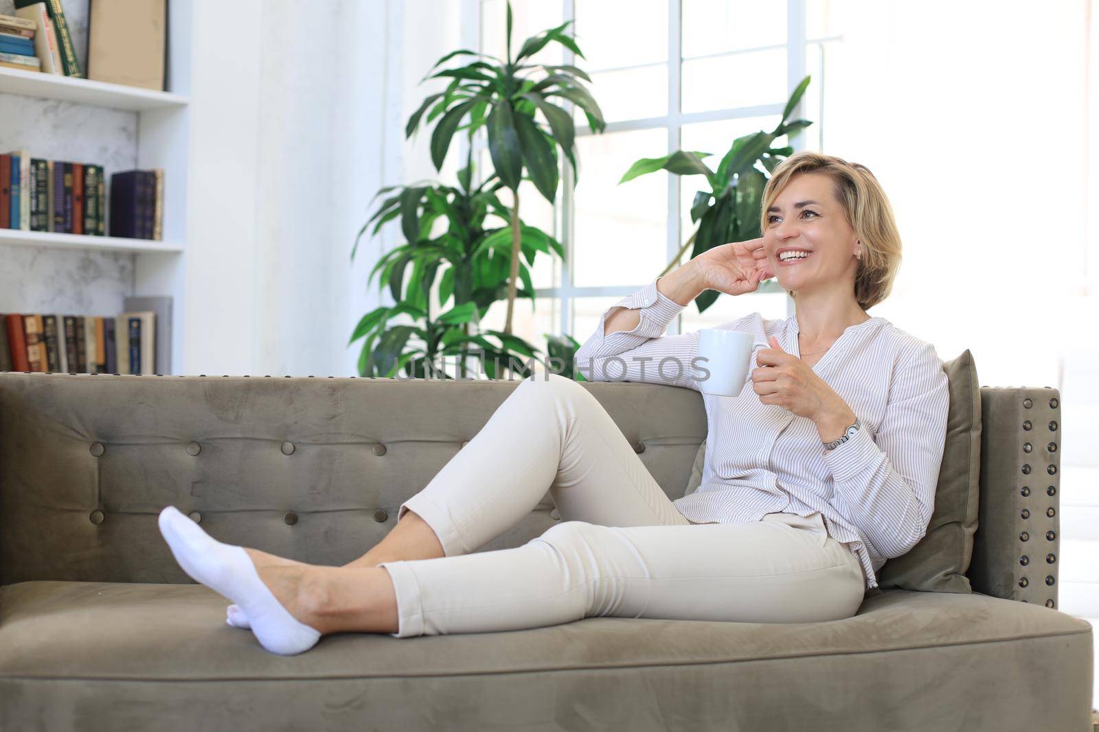 Mature blond woman in couch having a tea or coffee