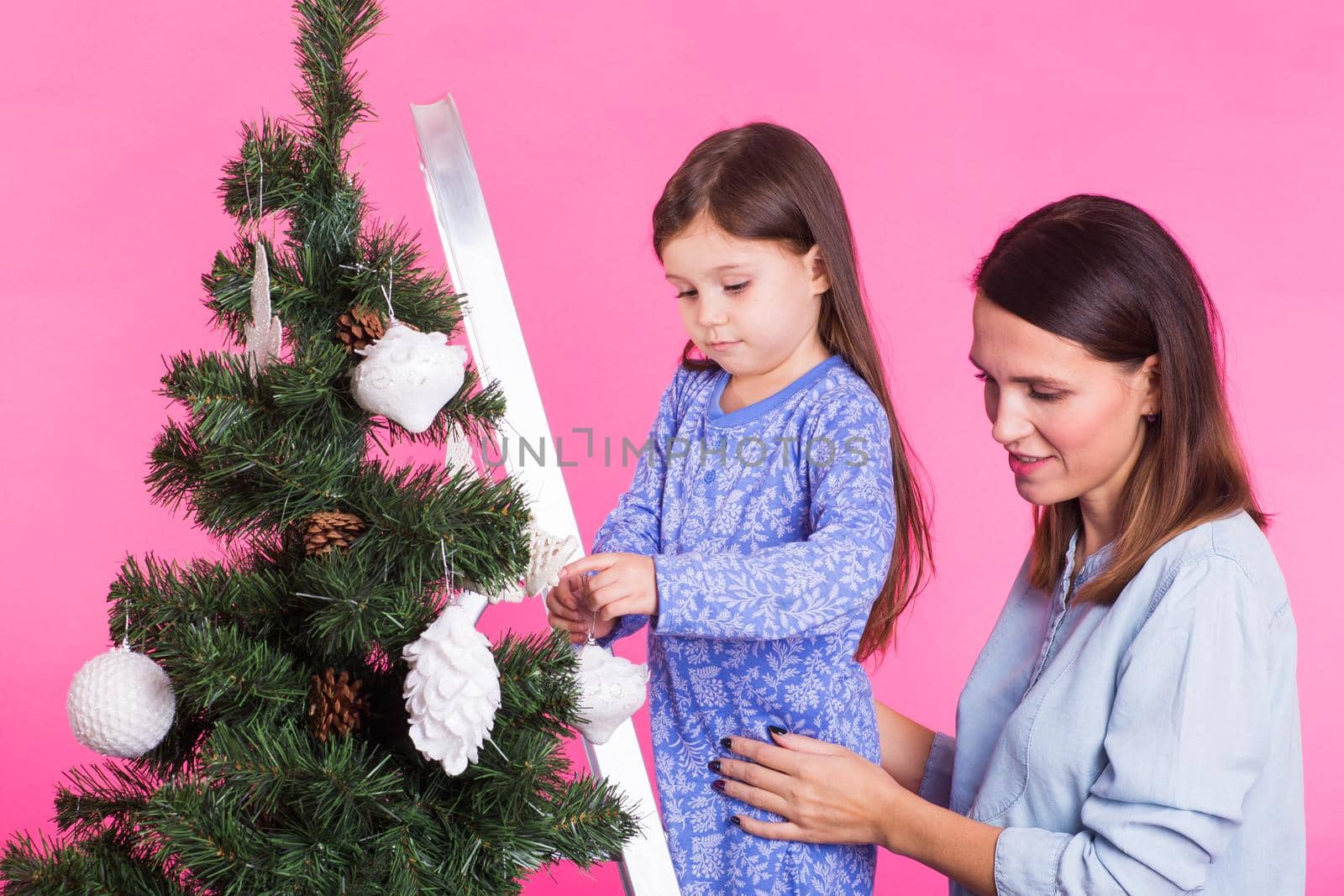 Christmas, childhood and people concept - child girl standing on step-ladder decorating the christmas tree with her mother on pink background by Satura86