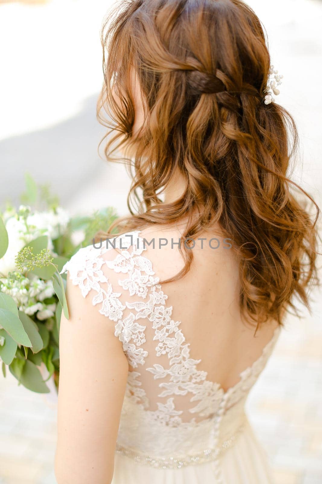 Back view of curls for bride keeping flowers. Concept of wedding photo session and stylish hair do.