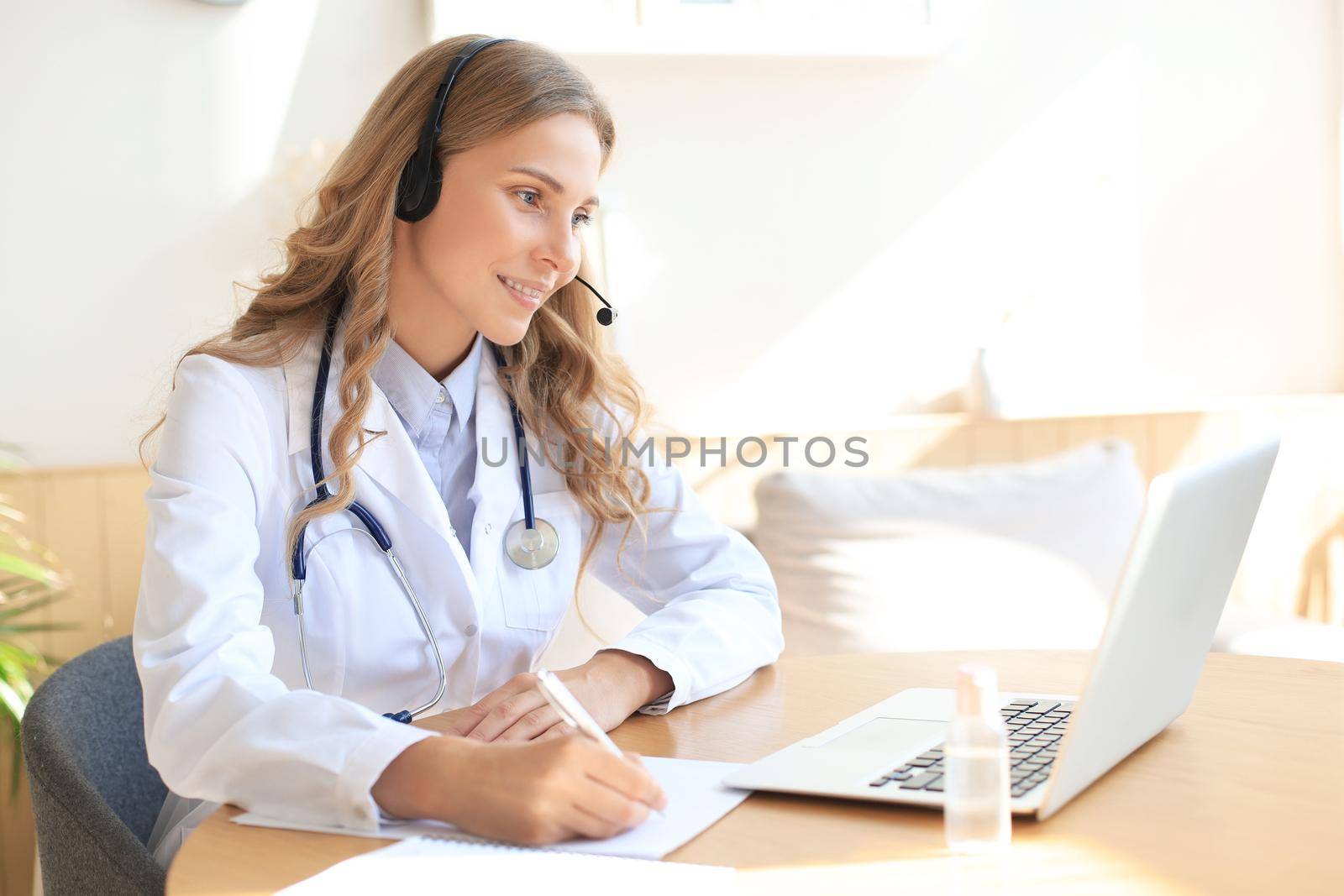 Friendly doctor working online with a laptop sitting in a desk in a consultation