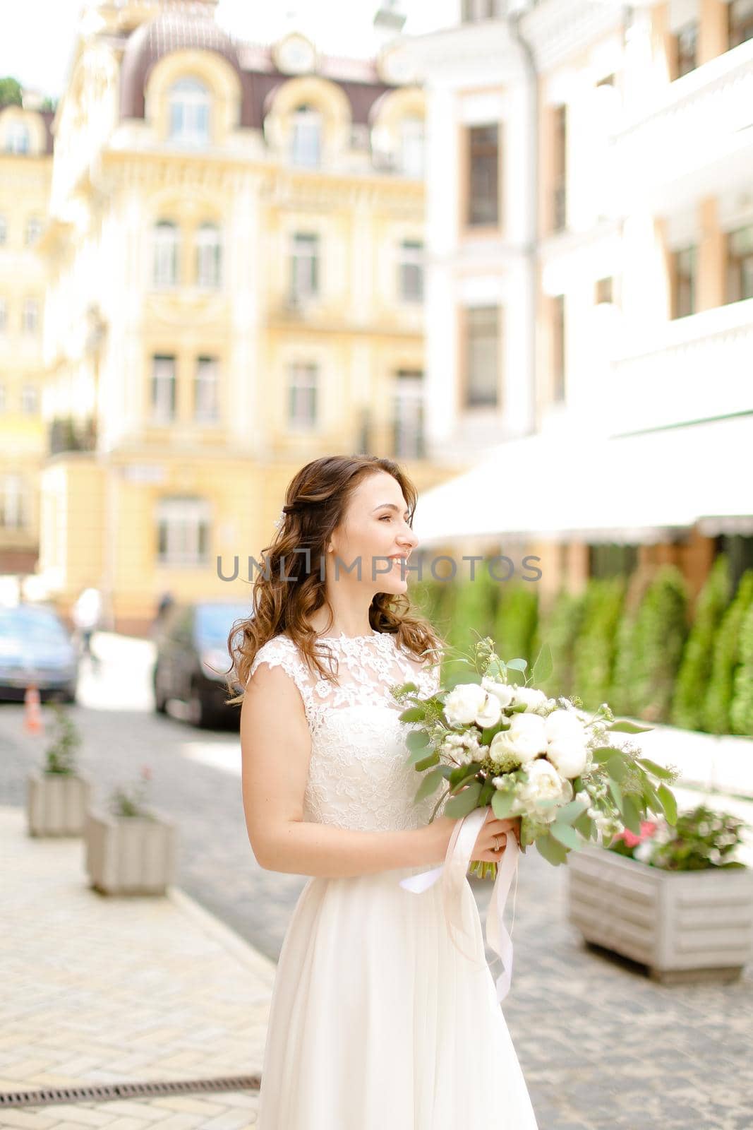 Caucasian charming fiancee walking with bouquet of flowers in city. Concept of bridal photo session.