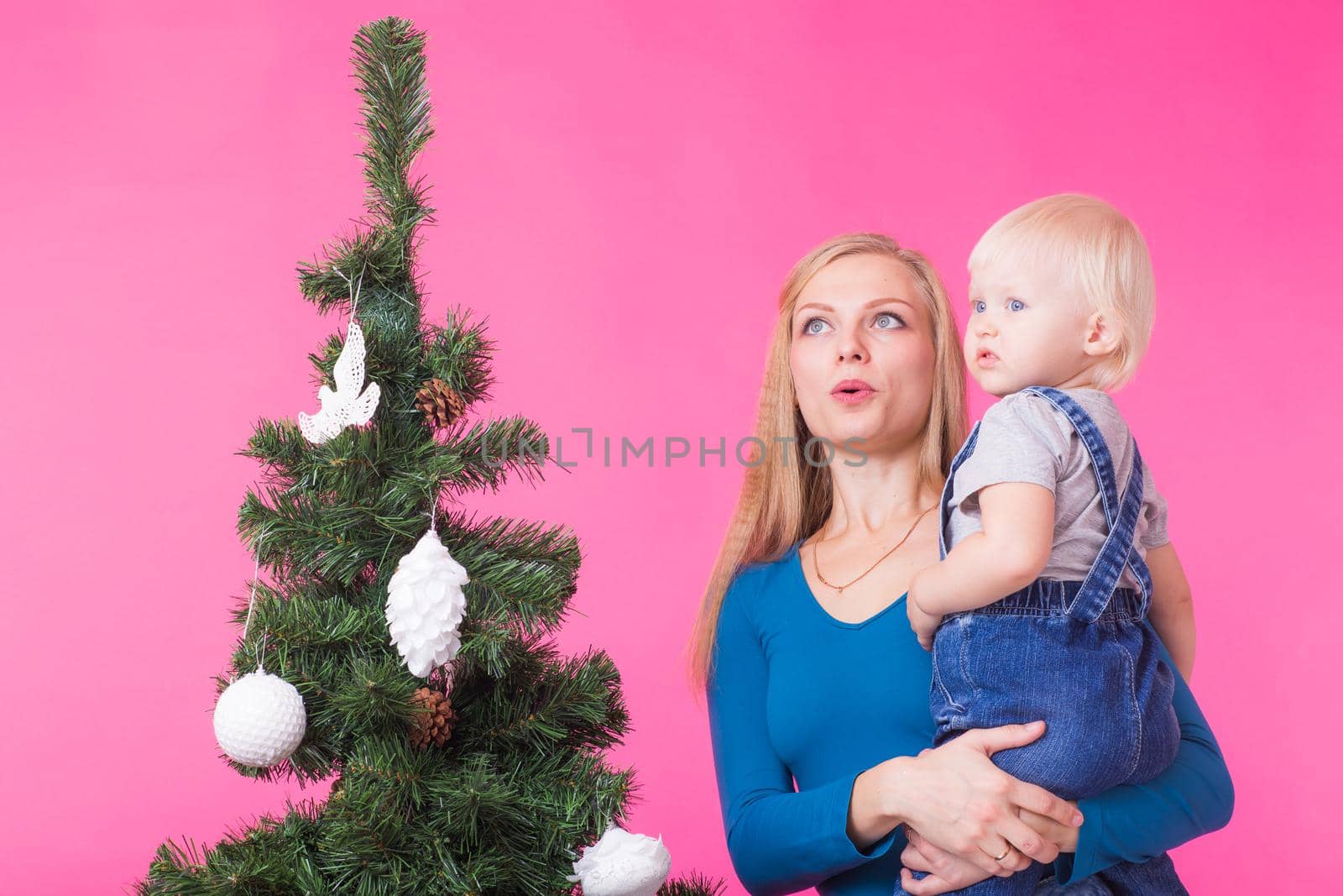 Holidays and people concept - Woman and her kid near christmas tree on pink background.