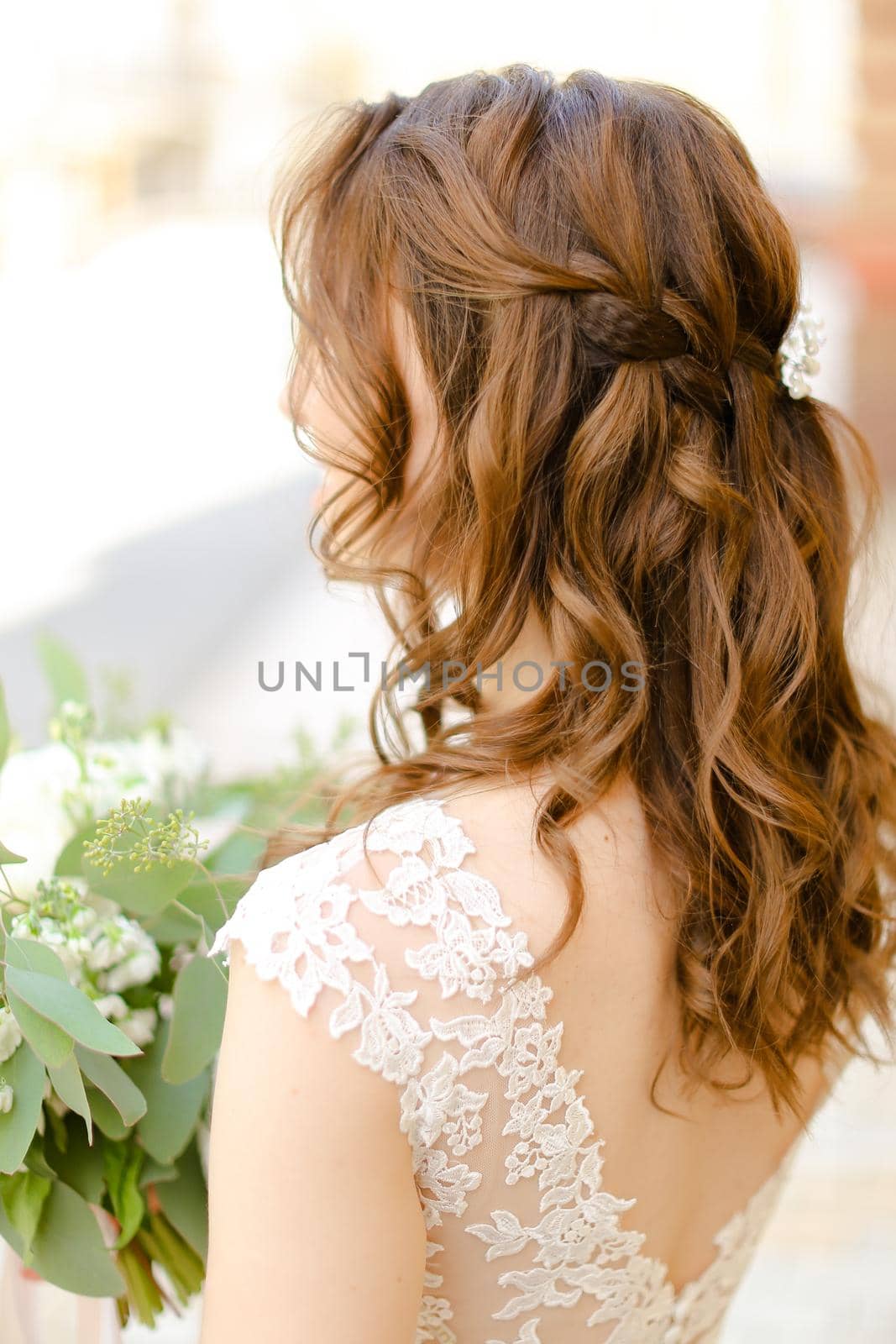 Back view of cute curls for bride keeping flowers. Concept of wedding photo session and stylish hair do.