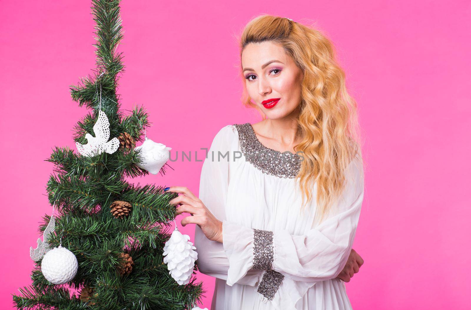 Christmas and holiday concept - Portrait of smiling beautiful blonde woman with Christmas tree on pink background.