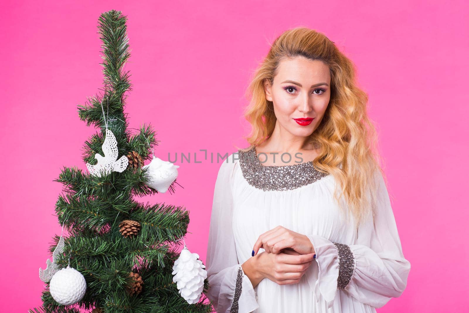 Christmas, holidays and people concept - young happy woman near christmas tree on pink background.