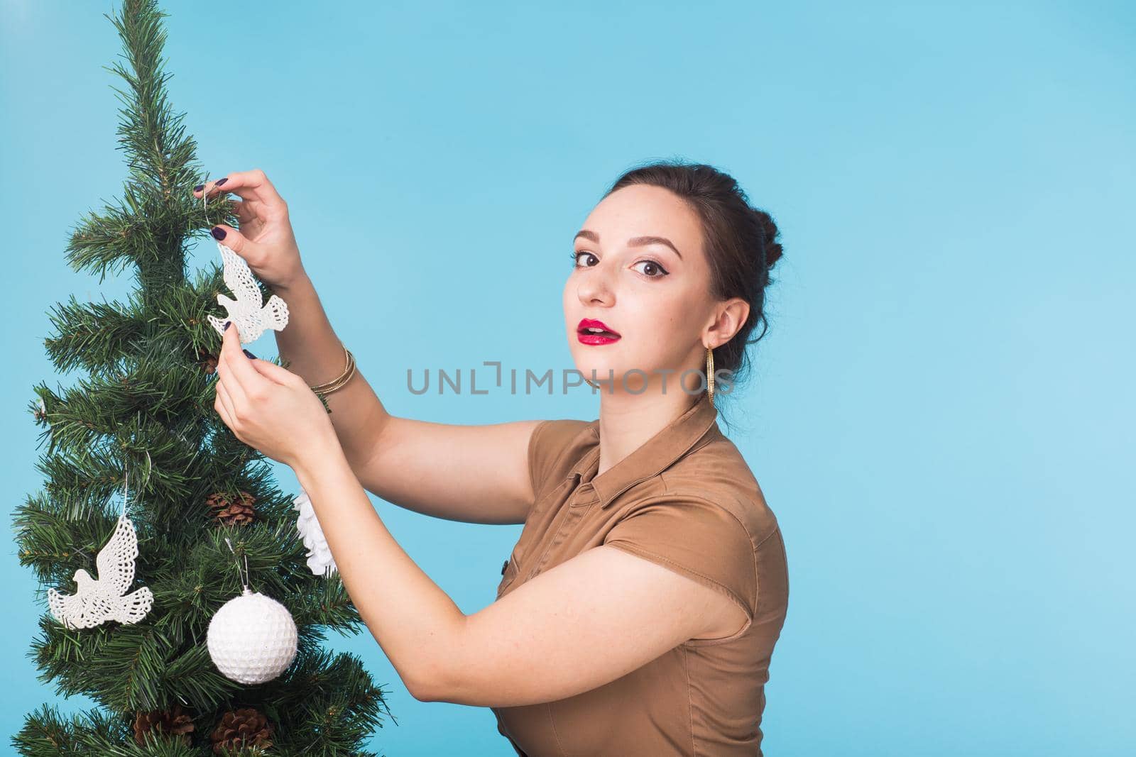 Christmas, holidays and people concept - young happy woman decorating christmas tree on blue background.