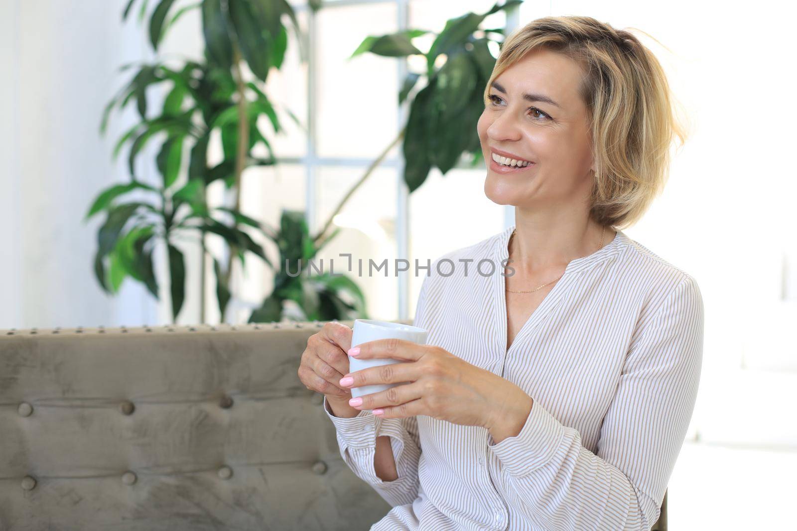 Mature blond woman in couch having a tea or coffee