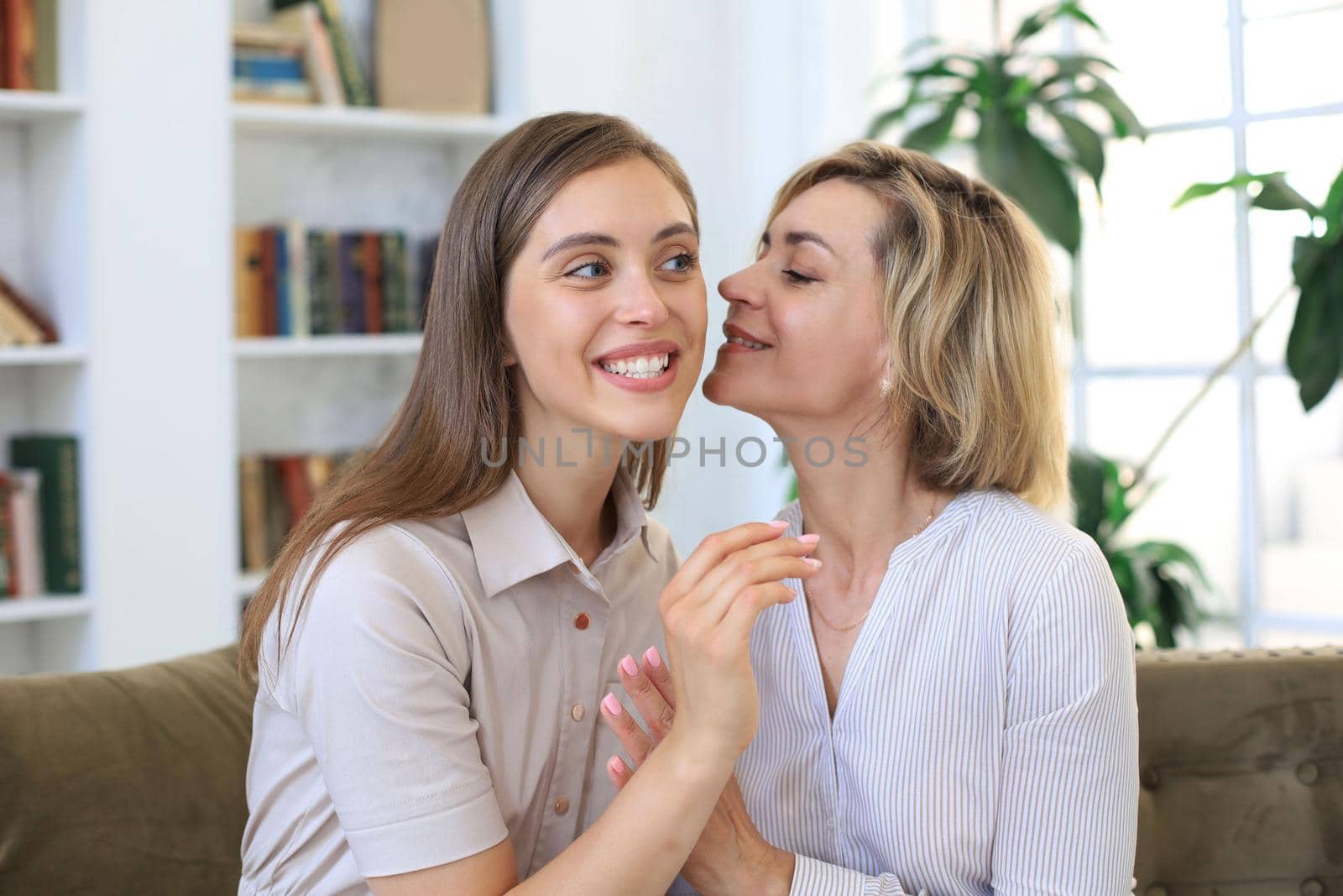 Happy middle aged mother and daughter talking on sofa in living room