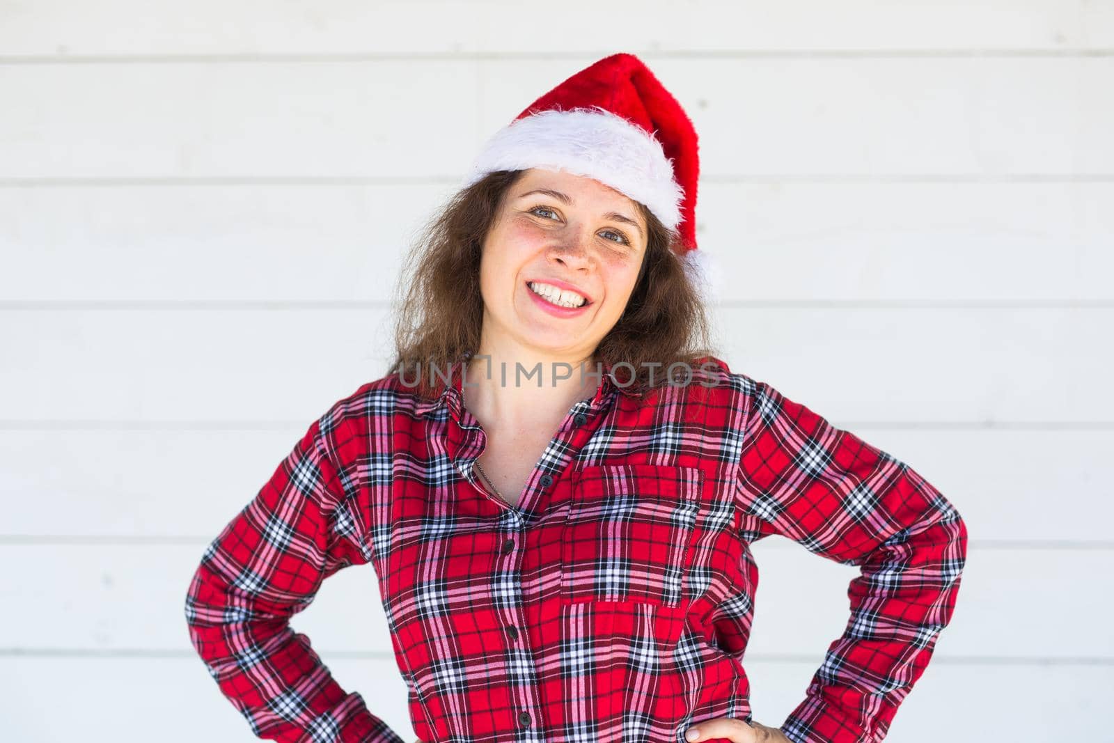 Holidays, christmas and clothing concept - pretty young woman in santa hat posing on white background by Satura86