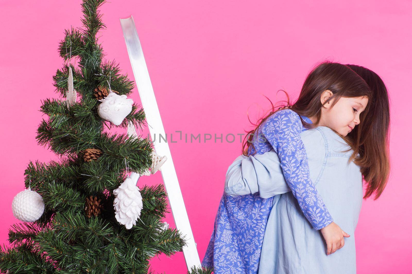 Christmas of young mom and her daughter with Christmas tree on pink background.