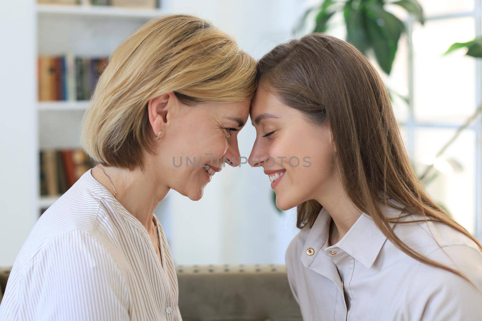 Happy middle aged mother and daughter talking on sofa in living room