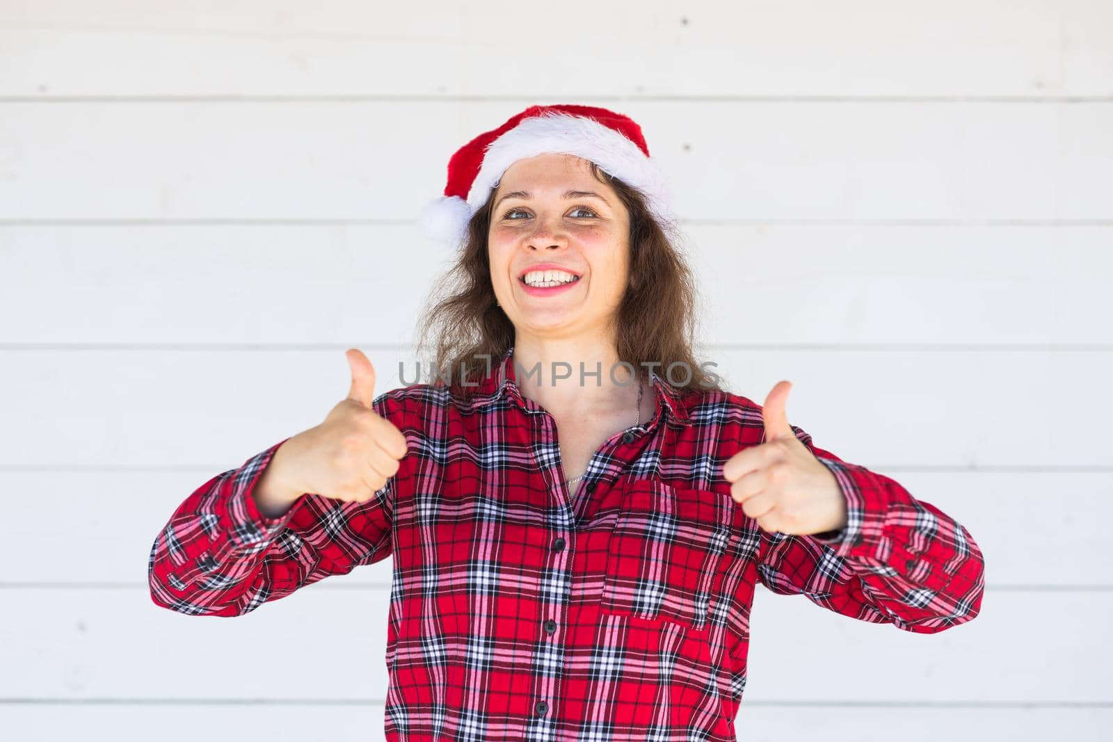 Christmas and people concept - woman in christmas hat showing thumbs up.