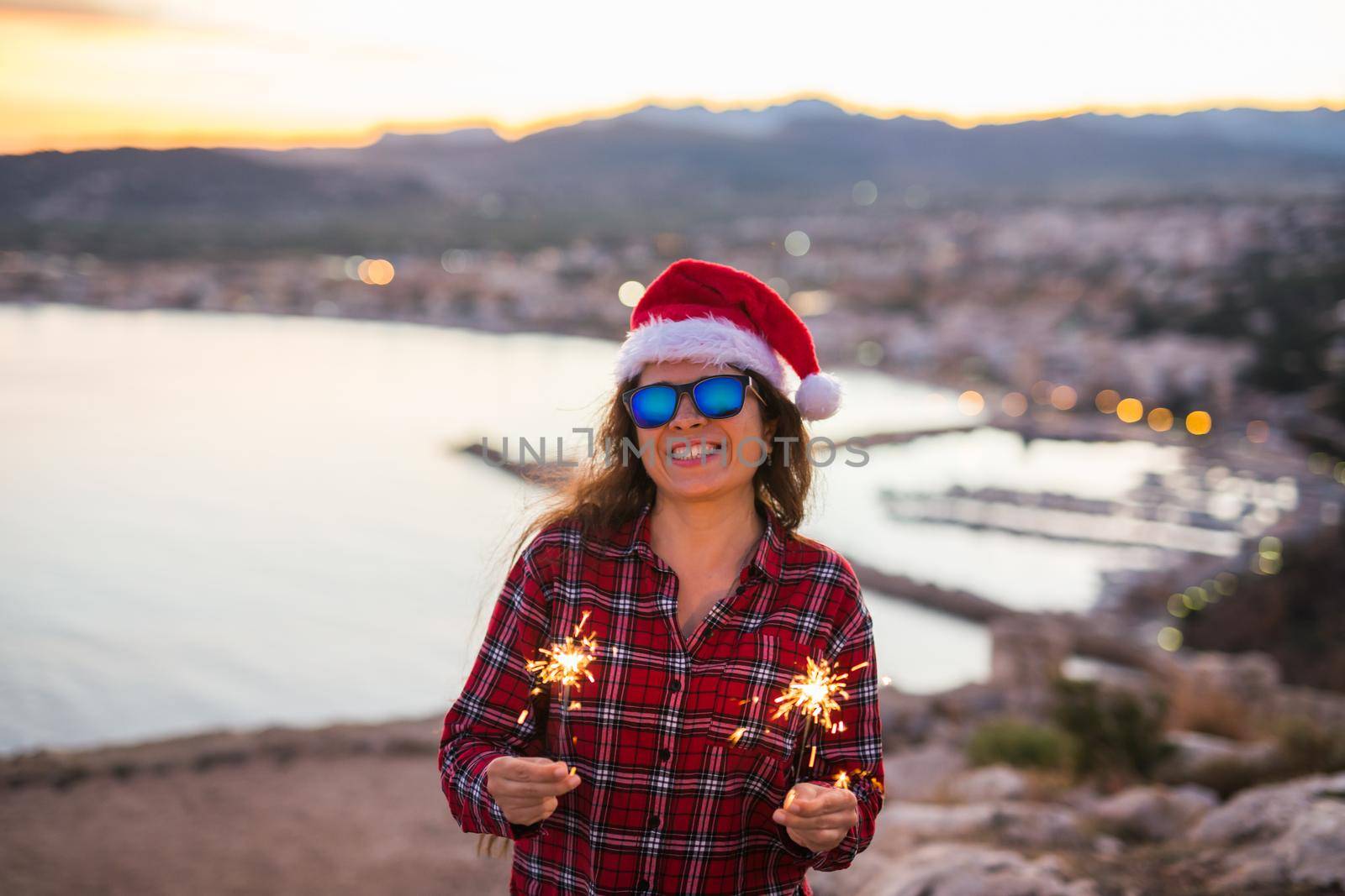 Holiday, Christmas and people concept - Young happy woman in Santa hat over beautiful landscape with fireworks and sparklers by Satura86