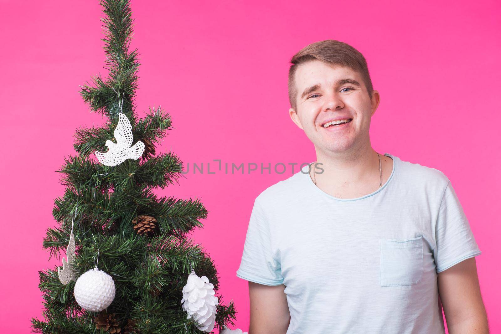 people, holidays and christmas concept - young smiling man near christmas tree on pink background.