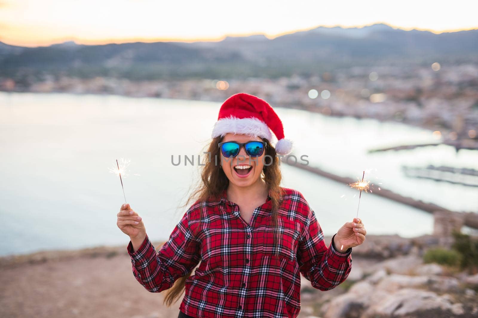 people, beauty and christmas concept - beautiful woman in glasses and hat holding sparkles.
