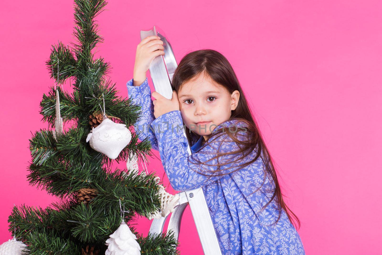 Children, holidays and christmas concept - little girl near christmas tree on pink background by Satura86