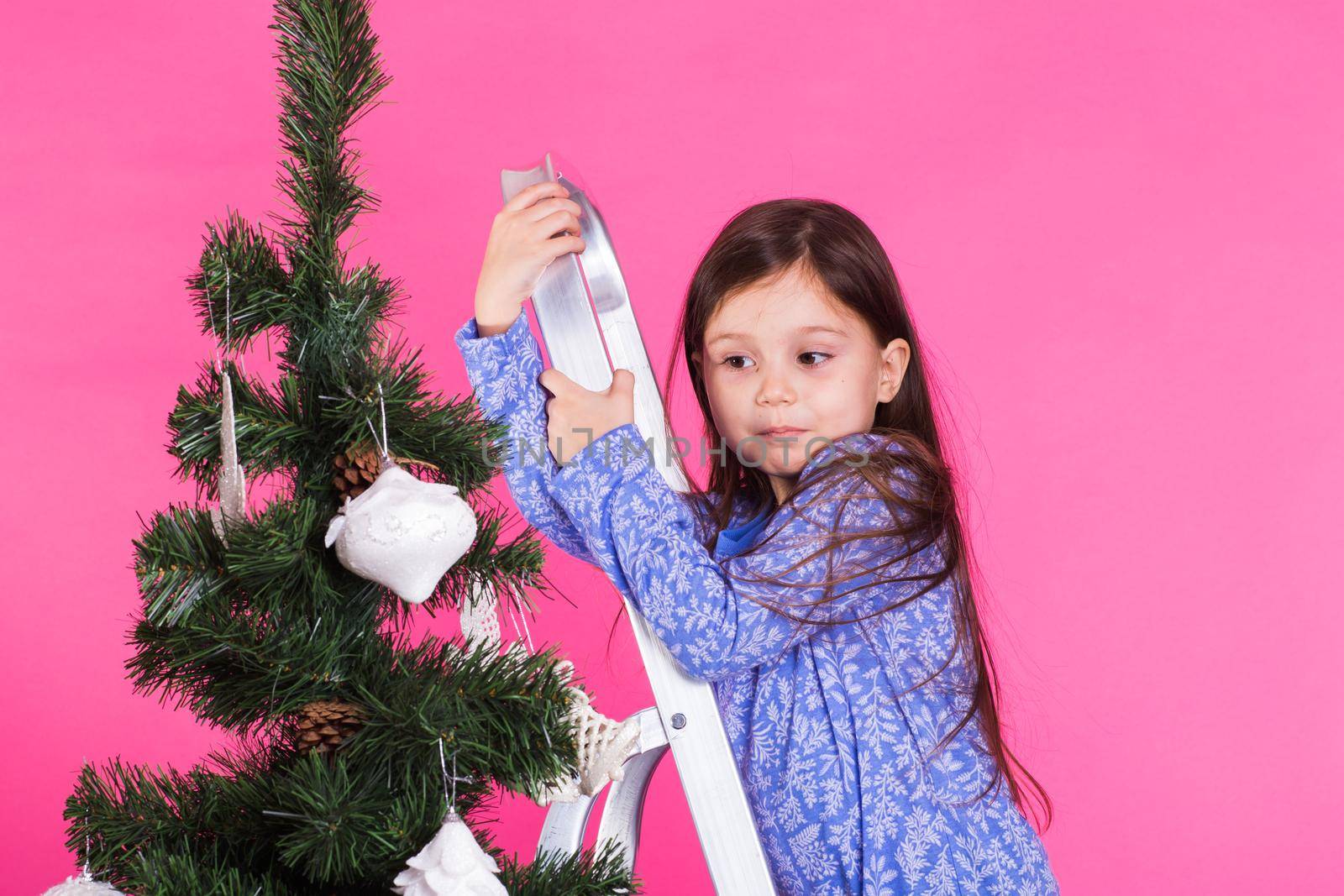 Children, holidays and christmas concept - little girl decorating christmas tree on pink background by Satura86