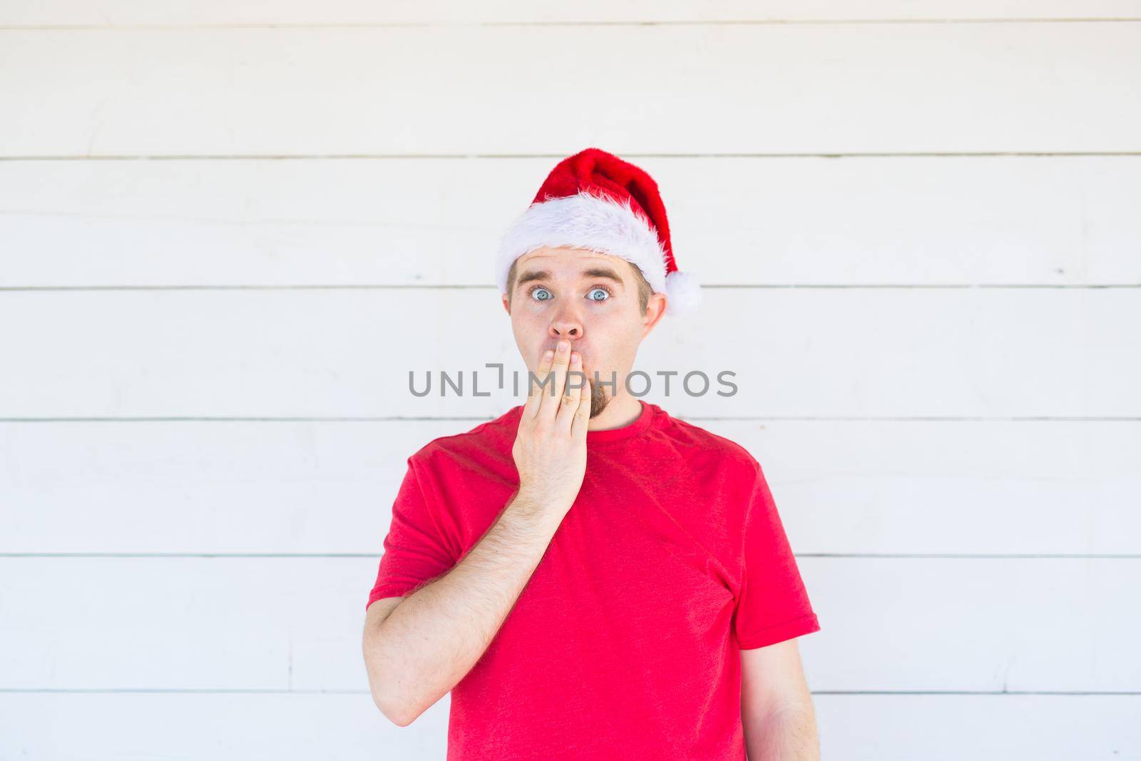 people, emotions and christmas concept - young surprised man in santa claus costume on white background.
