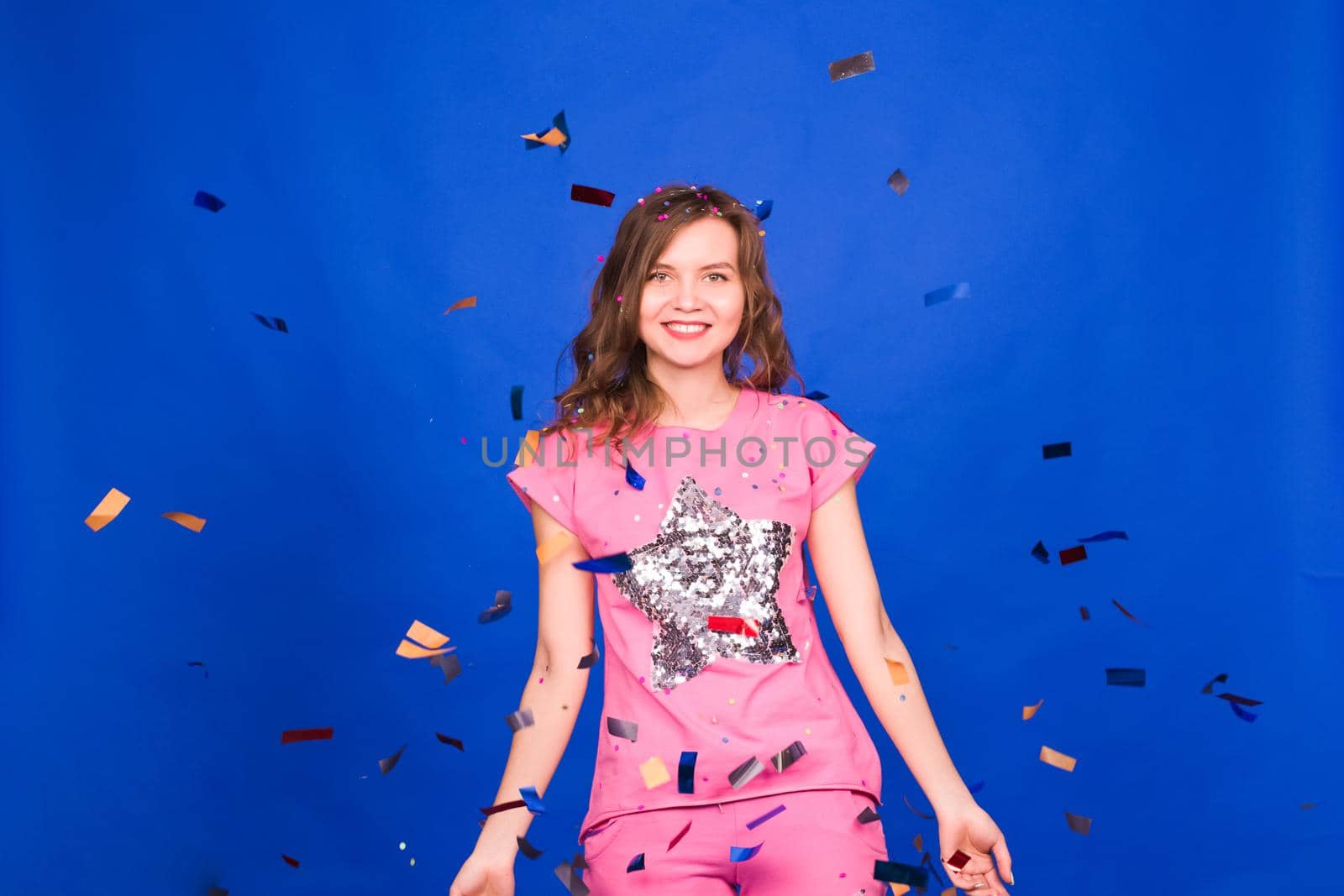 Beautiful happy woman at celebration party with confetti falling everywhere on her. Birthday or New Year eve celebrating concept.